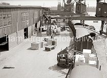 556_394a Blick von einem Hafenkran auf das geschftige Treiben im Hamburger Hafen. Kisten stehen zum Abtransport bereit - ein fahrbarer Schuppenkran hat gerade eine Holzkiste auf dem offenen Gterwaggon abgesetzt. Im Hintergrund werden Kisten und Ballen auf die Anhnger der Elektrokarren geladen.