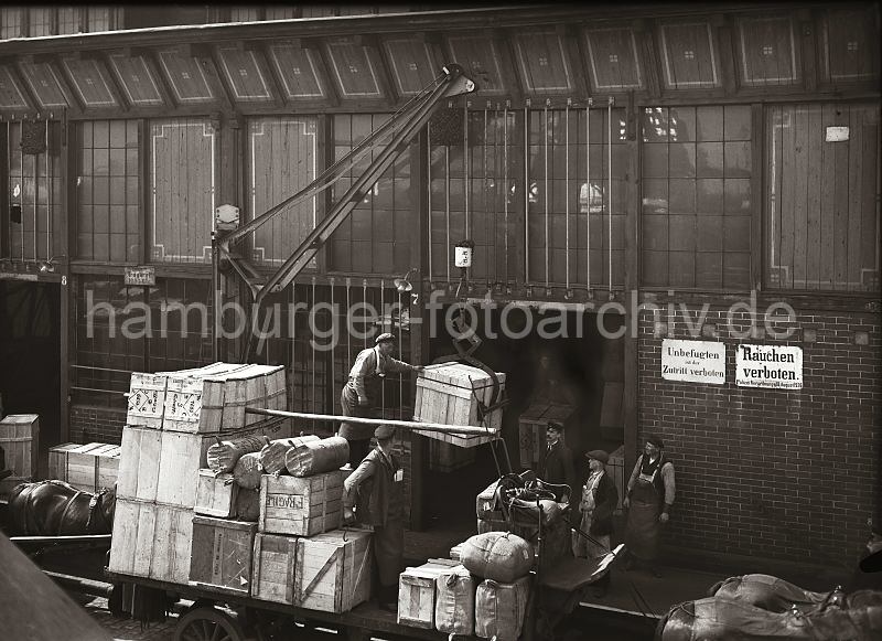Alte Hamburger Fotografien von der Arbeit im Hafen; Bild. Beladung eines Pferdefuhrwerks - fahrbarer Kran, Kistentransport mit Kistengreifer. Hamburg Bilder als Geburtstagsgeschen. 563_61 Pferdefuhrwerke stehen an der Laderampe eines Lagerschuppens im Hamburger Hafen; der Anhnger ist hoch mit Kisten und Ballen beladen. Ein fahrbarer Schuppenkran hebt gerade mit Hilfe eines Kistengreifers als Ladegeschirr eine Holzkiste von der Rampe an. Im Hintergrund stehen Lagerarbeiter, die mit weiteren Kisten auf ihren Sackkarren darauf warten, an die Reihe zu kommen.