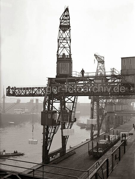 Alte Hamburgbilder von der im Hafenarbeit; Bildarchiv der HHLA. Dreifachkran  Schuppen 83 -Chilekai, Oderhafen. Hamburg fotos als Geburtstagsgeschenk. 564_183 Ein Dreifachkran transportiert vor dem Hafenschuppen 83 im Hamburger Oderhafen drei Kisten an Land. Vor der Laderampe steht ein offener Gterwaggon beladen mit Kisten - auf der Rampe ein Elektrohubwagen und Sackkarren. 