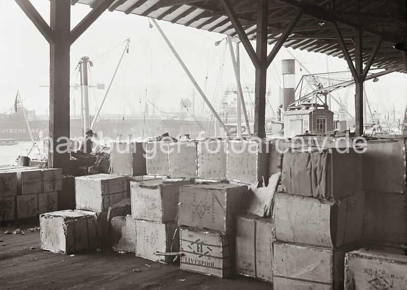 Praesent zum Abschied von Mitarbeitern. Hamburgfotos: Bilder von der Arbeit im Hafen Hamburgs - Kistenlagerung im Kaischuppen - Werftanlagen der Deutschen Werft. 570_652a Kisten mit Kautschuk mit der Aufschrift Smoked Sheet sind  in dem Lagerschuppen gestapelt. Auf anderen Holzkisten steht der Ursprungsort Liverpool. Im Hintergrund sind auf der anderen Seite der Elbe die Werftanlagen der Deutschen Werft zu erkennen.