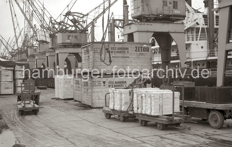 Bilder von der Geschichte der Technik im Hafen. Beladung eines Frachters im Kaiser-Wilhelm-Hafen/Kronprinzkai; Elektrokarren mit Anhnger. 575_3 Ein Frachter wird am Kronprinzkai des Kaiser-Wilhelm-Hafens beladen. Dicht an dicht stehen die Hafenkrane der Herstellerfirma Kampnagel am Kai und hieven die Ladung an Bord des Schiffs; lks. schweben Holzkisten ber dem Fahrer des Elektrokarrens - in der Bildmitte wird gerade das Tau, mit dem eine Ladung an Bord gebracht wurde wieder herabgelassen. Ein Hafenarbeiter macht gerade eine Hieve, die auf Anhngern der Elektrokarren liegt, fertig, damit sie an Bord des Frachtschiffs gebracht werden kann.
