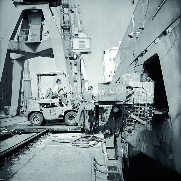 Geschichte der Arbeitstechnik im Hamburger Hafen Bilder aus dem Fotoarchiv der HHLA - Gabelstapler der HHLA beldt einen Frachter; ca. 1972.  577_03 Der Fahrer eines Gabelstaplers fhrt auf die Laderampe auf dem Kai und schiebt eine Palette mit Kisten durch eine Luke in der Seitenwand des Frachters.