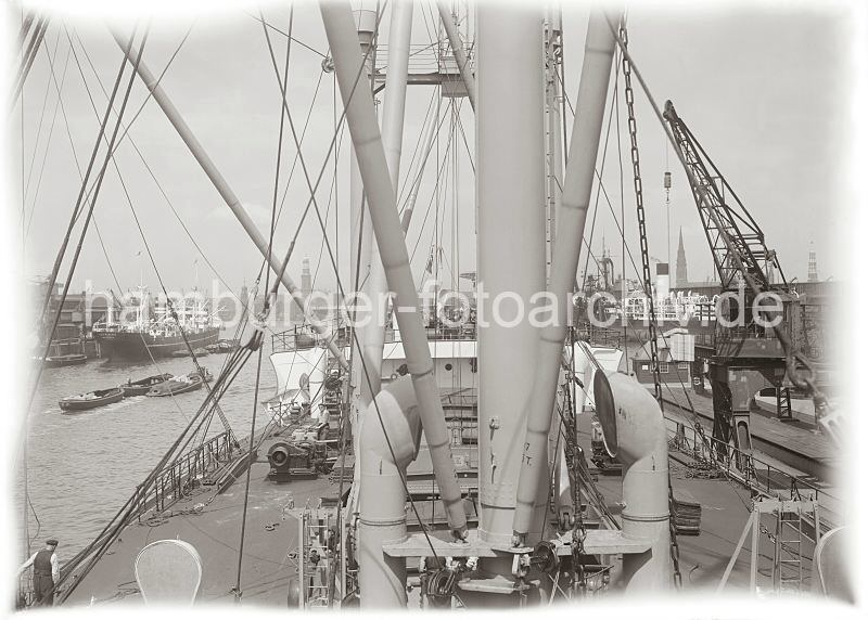 Historische Fotografien aus dem Fotoarchiv der HHLA. Frachtschiff am Australiakai des Indiahafens - Schuten im Hafenbecken.  582_660 Blick ber das Deck eines Frachters im Indiahafen - rechts lscht ein Kran die Fracht. Im Hintergrund sind die Kirchtrme von drei Hamburger Hauptkirchen St. Michaelis, St. Nikolai und St. Katharinen zu erkennen. Am gegenber liegenden Afrikakai wird die Ladung eines Frachtschiffs gelscht - im Hafenbecken werden drei beladene Schuten von einem Schlepper Richtung Elbe geschleppt.