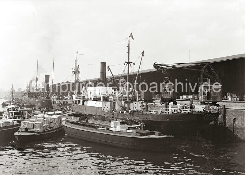 Alte Hafenfotos aus dem Bildarchiv der Hamburger Hafen und Logistik AG (HHLA. Frachtschiffe und Schuten im Grasbrookhafen / Dalmannkai; ca. 1932. 601_670a Frachter liegen am Dalmannkai des Hamburger Grasbrookhafens - die Ladung wird auf Schuten gelscht und ber auf Schienen laufende Hafenkrane an Land gebracht. Im Hintergrund werden die angelandeten Gter im Kaischuppen15 des Grasbrookhafens gelagert.