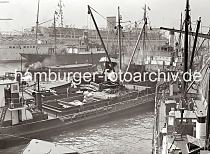610_387 Ein Motorschiff wird vor den Kaianlagen an den Vorsetzen / Baumwall mit Scken beladen. Am bordeigenen Ladebaum hngt eine Ladung Scke, die von der lngsseits liegenden Schute geholt wurde. ber den Ausleger des Kaikrans wird der vordere Laderaum des Schiffs befrachtet. Im Hintergrund liegt das 1938 gebaute NS-Passagierschiff Wilhelm Gustloff am Ponton. 