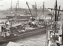 610_387 Ein Motorschiff wird vor den Kaianlagen an den Vorsetzen / Baumwall mit Scken beladen. Am bordeigenen Ladebaum hngt eine Ladung Scke, die von der lngsseits liegenden Schute geholt wurde. ber den Ausleger des Kaikrans wird der vordere Laderaum des Schiffs befrachtet. Im Hintergrund liegt das 1938 gebaute NS-Passagierschiff Wilhelm Gustloff am Ponton. 