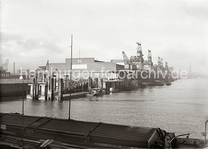 Historische Hafendokumente aus dem Bildarchiv der Hamburger Hafen und Logistik AG. Verteilungsschuppen 60 am Kamerunkai des Sd-West-Hafens - Hafenkrane an der Kaianlage. 616_638a Blick vom Windhukkai des Sdwesthafens zum Schuppen 60 am damaligen Afrikakai - eine Barkasse legt gerade vom Ponton des Anlegers ab. Unter den Halbportalkranen stehen die Waggons eines Gterzugs - lks. im Hintergrund Industriegebude am Reiherstieg, re. der Turm der St. Nikolaikirche.