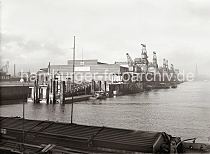 616_638a Blick vom Windhukkai des Sdwesthafens zum Schuppen 60 am damaligen Afrikakai - eine Barkasse legt gerade vom Ponton des Anlegers ab. Unter den Halbportalkranen stehen die Waggons eines Gterzugs - lks. im Hintergrund Industriegebude am Reiherstieg, re. der Turm der St. Nikolaikirche.