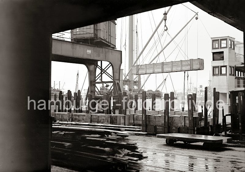 Historische Hafen-Bilder aus dem Fotoarchiv der Hamburger Hafen und Logistik AG HHLA - Gueterumschlag am Kai - Holzkisten auf Gterwaggons - Verladung einer Holzkiste.  622_20_B_255a Ein offener Gterzug fr Stckguttransport steht an der Laderampe, die Gterwagen sind mit langen Holzkisten beladen; die Ladung auf den Flachwagen sind mit Rungen gesichert, die auch ein hheres Stapeln der Fracht ermglichen . Eine der Kisten hngt an einem Kranhaken ber dem Hafenkai.