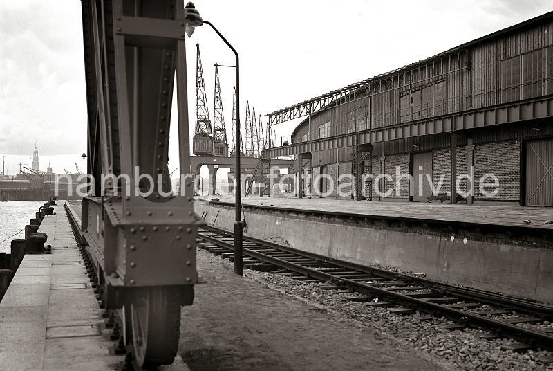 Alte Fotografien von der Arbeit im Hafen Hamburgs. Laufrder eines Halbportalkrans am Togokai / Sdwesthafen.  622_22_B_246 Die Laufrder des Halbportalkrans werden auf Schienen gefhrt, die auf der Kaimauer des Togokais verlaufen - das andere Ende des Portals wird an einem Eisengerst an der Fassade des Schuppens 58 gefhrt. Im Hintergrund sind der Turm des Hamburger Michel und rechts davon die Spitze des Kaispeichers A zu erkennnen.