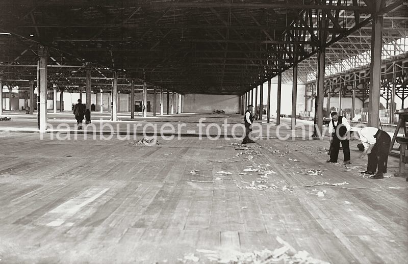 Historische Arbeitsmotive aus Hamburgs - Bilder aus dem Archiv der HHLA: Erweiterungsarbeiten am  Verteilungsschuppen 57 /58. 622_24_B_207a Der Verteilungsschuppen 58 als Erweiterungsbau des Schuppen 57 ist fertig gestellt; Zimmerleute arbeiten am Holzboden des Lagerschuppens, whrend ein anderer Arbeiter mit einem Reisigbesen den Boden reinigt. Rechts hinter der Gleisanlage der Hafenbahn ist der alte Schuppen 57 mit Lagergut zu erkennen.