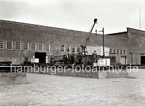 622_26_B_253a An einer der Laderampen des Verteilungsschuppens 58 am Togokai des Hamburger Sdwesthafens wird ein Lastkraftwagen mit Anhnger entladen. Ein mobiler Schuppenkran hebt eine groe Holzkiste vom Anhnger eines LKW - ein Elektrokarren mit Anhnger auf dem sich eine weitere Kiste befindet steht bereit, die schwere Ladung aufzunehmen und in den Schuppen zu transportieren.