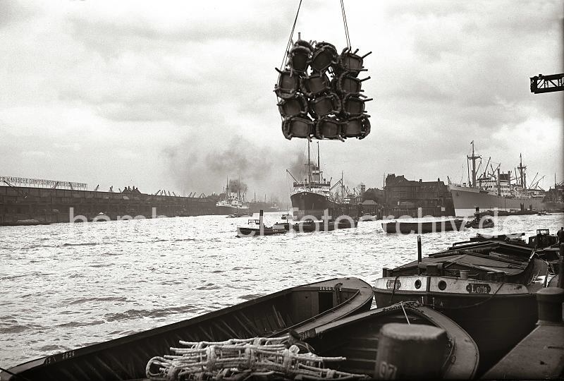 Alte Hafenbilder aus Hamburg.Gterumschlag im Indiahafen Kamerunkai - Blick zum Hansahft / Hansahafen. 622_28_B_247a Eine Schute ist mit verpackten Rohrsthlen beladen - eine Ladung Sthle hngt ber dem Schiff an dem Kranhaken am Kamerunkai des Hamburger Indiahafens. Im Hintergrund rechts hat ein Frachter vor dem Schuppen 52 des Australiakais festgemacht. Ein Schlepper zieht eine Schute in der Mitte des Hafenbeckens; in der Bildmitte das Hansahft und der Frachter HALLE am Kai. Links ist ein Teil des Schriftzugs "Hamburg Sdamerikanische Dampfschifffahrts- Gesellschaft" auf den Dchern der Kaischuppen 46 + 47 am O'swaldkai des Hansahafen zu lesen. 