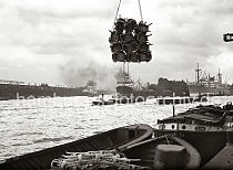 622_28_B_247a Eine Schute ist mit verpackten Rohrsthlen beladen - eine Ladung der Fracht hngt ber dem Schiff am Kran des Kamerunkai vom Hamburger Indiahafen. Im Hintergrund rechts hat ein Frachter vor dem Schuppen 52 des Australiakais festgemacht. Ein Schlepper zieht eine Schute in der Mitte des Hafenbeckens; in der Bildmitte das Hansahft und der Frachter HALLE am Kai. Links ist ein Teil des Schriftzugs "Hamburg Sdamerikanische Dampfschifffahrts- Gesellschaft" auf den Dchern der Kaischuppen 46 + 47 am O'swaldkai des Hansahafen zu lesen. 