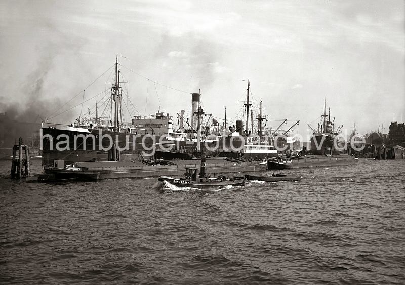 Alte Hafenfotografien aus Hamburg. Frachtschiffe und Binnenschiffe an Dalben im Indiahafen - Blick zum Hansahft / Hansahafen.  22_29_B_131 Blick vom Afrikahft; der Schlepper "Carl Lorenz" zieht einen Kahn dessen Schiffer mit verschrnkten Armen an Bord sitzt und die Fahrt durch den Hafen Hamburgs geniesst. An den Dalben des Indiahafens liegen zwei Binnenschiffe, das Motorschiff AMBRIA und der Frachter TENERIFE.  Rechts im Hintergrund das Hansahft und am Bremer Kai des Hansahafens der Frachter KARNAK?.