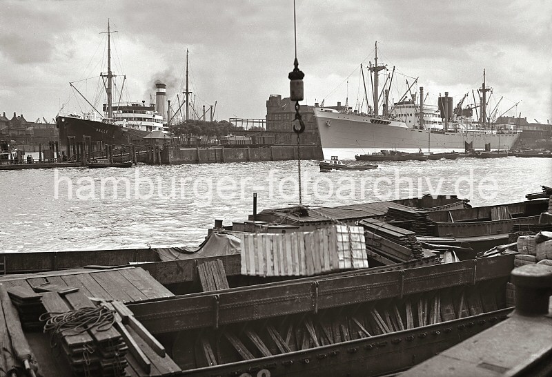 Historische Hamburg - Fotos aus dem Bildarchiv der Hamburger HHLA. Frachtschiffe und Schuten im Indiahafen - Anleger am Hansahft / Hansahafen. 623_B_247 Schuten liegen am Togokai des Indiahafens, ihre Ladung wird gelscht. An einem Kranhaken hngt eine Hieve Kisten. Auf der gegenberliegenden Seite des Hafenbecken hat das Frachtschiff WELTEVREDEN am Austrliakai festgemacht - Schuten liegen lngsseits. Links der Anleger vom Hansahft, eine Hafenfhre legt ab, deren Passagiere gehen die eiserne Wassertreppe hinauf. Dahinter das Frachtschiff HALLE im Hansahafen.