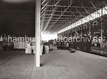 627_B_246a Geschlossene Gterwaggons stehen in der Mitte des Lagerschuppens, in dem die Ware zumeist in Holzkisten  zum Schutz beim Transport sicher verpackt ist. Ein leerer Elektrokarren  und Lagerarbeiter stehen vor einem der gedeckten Gterwagen -  ber einem der Puffer ist das Schild AUSTAUSCHBAU angebracht. 