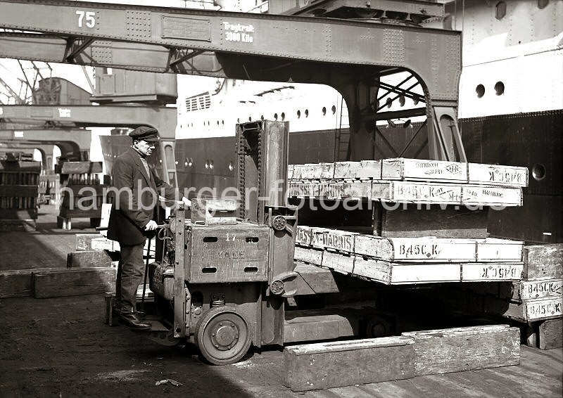 Historische Hamburg-Bilder aus dem Fotoarchiv der Hamburger Hafen und Logistik AG - Hubwagen mit Fahrertransportiert Holzkisten - Hafenkai, Frachtschiff. 629_72 Arbeitserleichterung durch den Einsatz eines Akku-Hubstaplers auf einer Kaianlage des Hamburger Hafens. Der Fahrer stapelt groe Holzkisten fr die Verladung auf das lngsseits liegende Frachtschiff bereinander.