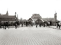 643_B_280a Es scheint Feierabend zu sein bei den Angestellten und Arbeitern in der Speicherstadt. Mnner und Frauen gehen ber die Niederbaumbrcke, die ber den Zollkanal fhrt. Ein Schild an einer der Laternen weist auf den Zollgrenz-Bezirk hin. Einige Frauen mit Kindern warten auf ihre Mnner - im Hintergrund hinter den eisernen Brckenbogen ist das Dach der Polizeiwache zu erkennen, rechts der Kaispeicher A und lks. hinter dem Zollgebude einer der Giebeltrme der Speicherstadt.