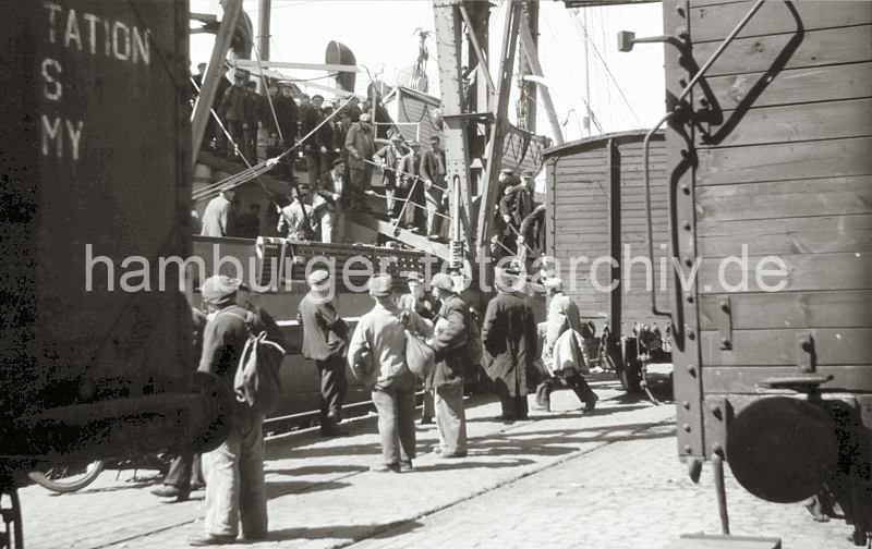 Historische  Bilder von der Arbeit im Hamburger Hafen aus dem Archiv der HHLA. Feierabend am Rokai des Rohafens - Hafenarbeiter verlassen das Frachtschiff; ca. 1948. 644_5 Feierabend bei Arbeitern im Hamburger Hafen - die Hafenarbeiter verlassen ber die Gangway den Frachter am Rokai. Die meisten Mnner tragen die typische Hamburger Schirmmtze, den "Elbsegler" und einen Zampel. In diesem Beutel tragen sie ihre Verpflegung fr den Arbeitstag.