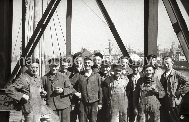 Historische  Bilddokumente von der Arbeit im Hamburger Hafen aus dem Archiv der HHLA. Schauerleute im Rohafen - Hafenarbeiter im Hamburger Hafen; ca. 1948.  646_3 Die Schauerleute im Rosshafen machen eine Pause, einige Haben eine Pfeife in der Hand, die meisten tragen einen "Elbsegler", die typische Hamburger Schirmmtze. Die Aufgabe der Schauerleute besteht im Stauen bzw. dem Be- und Entladen der Frachschiffe. Der Begriff Schauermann stammt vom niederlndischen Wort sjouwen = schleppen. Die Arbeiter im Hafen Hamburgs waren hufig Tagelhner, die zur Erledigung eines bestimmten Auftrags eingestellt wurden.