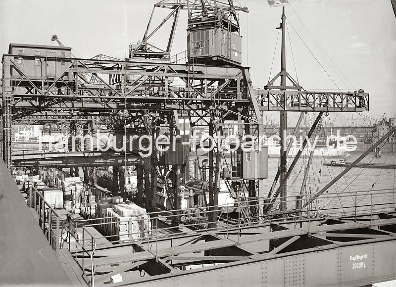 Dreifachkrne  am Chilekai des Hamburger Oderhafens - beladener Gterzug an der Laderampe; ca. 1934. Historische  Bilddokumente der Hafenarbeit im Hamburger Hafen.  650_541b Die Halbportale der Dreifachkrne berspannen die Kaiflche am Chilekai des Oderhafens; an der Laderampe steht ein Gterzug mit offenen Gterwaggons, die mit Kisten und Ballen beladen sind. Am Kai liegt ein Frachter, dessen Ladung mit Hilfe der Krne gelscht wird. Auf der gegenber liegenden Seite des Hafenbeckens liegt ein Frachtschiff am Mnckebergkai vor dem Schuppen 77.