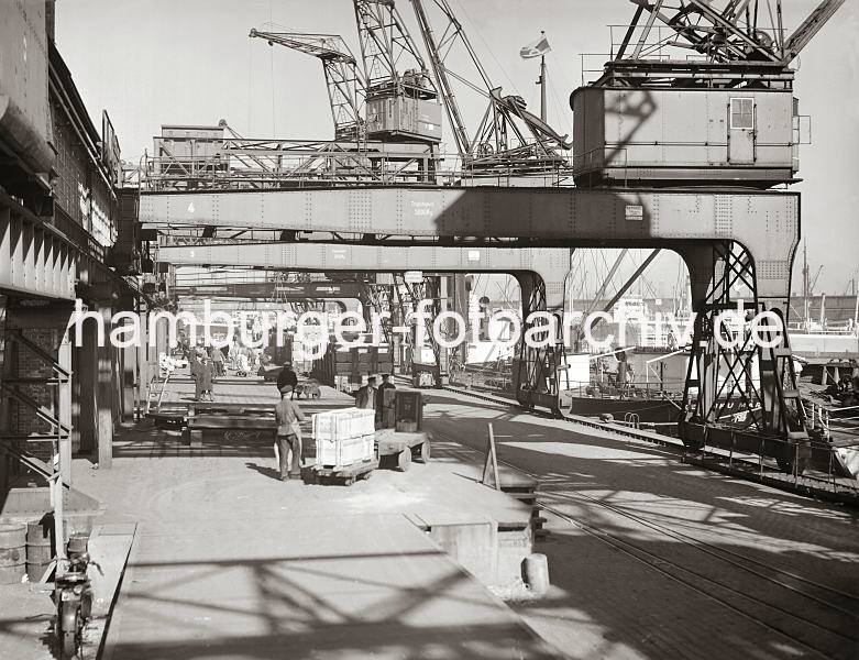 Laderampe am Chilekai im Hamburger Oderhafen, Elektrokarren mit beladenem Anhnger. Historische  Bilddokumente der Hafenarbeit im Hamburger Hafen. 653_542a Ein Elektrokarren steht auf der Laderampe des Chilekais im Hamburger Oderhafen. Zwei Holzkisten sind auf dem Anhnger des Transportfahrzeugs von den Kaiarbeitern gestapelt worden. An der Laderampe steht ein mit Paketen voll beladener Gterzug - eine Hieve mit Rollen wird gerade von einem Kran auf der Rampe abgesetzt. Kaiarbeiter transportieren die Ladung mit ihren Sackkarren in den Schuppen.