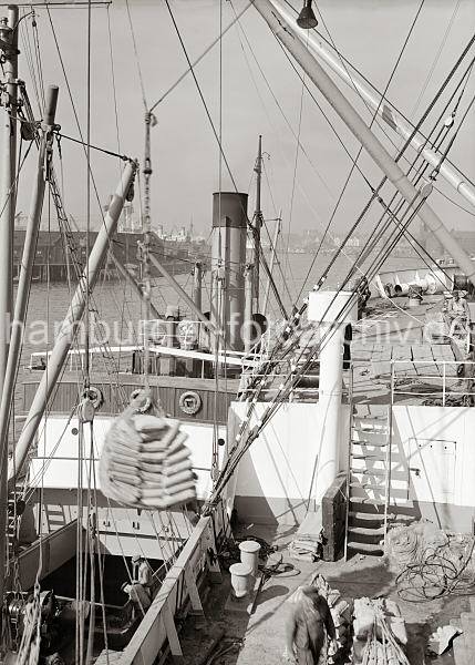 Geschichte vom Hamburger Hafen. Hafen-Geschichte; eine  Hieve Scke ber dem Laderaum des Frachters; ca. 1934. 658_684 Die Ladung eines Frachters wird im Hamburger Hafen gelscht. Eine Hieve Scke wurde gerade aus dem Laderaum des Frachtschiffs geholt und wird mit dem Kran an Land gebracht.