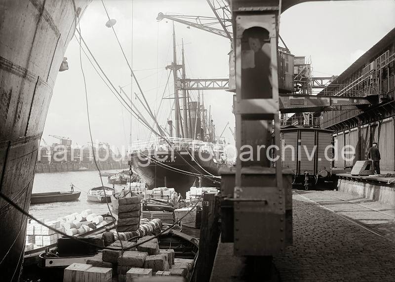 Geschichte des Hafen Hamburgs - historische Fotos aus dem Archiv der HHLA. Beladung einer Schute im Hamburger Hafen - Gterwaggon an der Laderampe des Kaischuppens; ca. 1934. 659_625 Ein Frachter lscht einen Teil seiner Ladung direkt in eine Schute, deren Laderaum mit Kisten und Ballen gefllt ist. Die Lastkhne haben keinen eigenen Antrieb sonder werden mit Bootshaken gestakt oder mit Hilfe eines Schleppers im Hafengebiet bewegt.