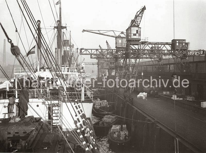 Bilder zur Geschichte des Hafen Hamburgs - historische Hafen Fotos. Abgebumter Frachter an einem Kai des Hamburger Hafens; ca. 1934.  660_3502_34 Ein Frachter wird mit Holzstmmen von der Kaimauer abgehalten (abgebumt), damit die Schuten zum Gterumschlag einen Liegeplatz bekommen. Teilweise wird die Ladung Jute und Baumwolle des Frachters auf der Laderampe des Kais abgesetzt oder direkt in die lngsseits liegenden Schuten verladen.