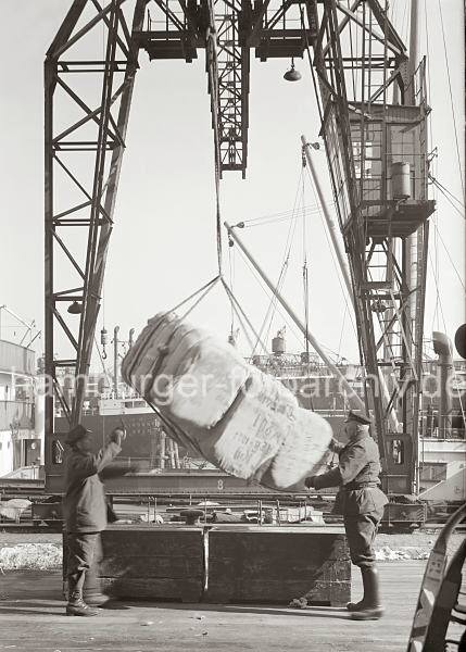 663_726 Die Ladung eines Frachters wird gelscht; der Hafenkran setzt drei Baumwollballen am Hafenkai ab. Die Kaiarbeiter nehmen die Hieve in Empfang - im Vordergrund wartet schon ein Arbeiter mit Sackkarre, um die Ware in den Kaischuppen zu transportieren. Bilddokumente zur Geschichte des Hamburger Hafens - historische Fotos Gterumschlag am Hafenkai; ca. 1934. 
