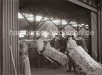 666_587 Kaiarbeiter transportieren dei Wollballen mit Sackkarren von der Laderampe in den Kaischuppen. Durch das Oberlicht des Lagerhauses fllt das Licht auf den mit Ballen gefllten grossen Raum.