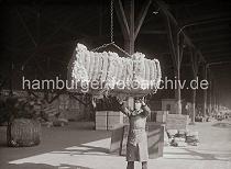 672_439 Ein Wollballen hngt im Ladegeschirr und wird von einem Hafenarbeiter am Kai angenommen. Im Hintergrund sind in dem offenen Schuppen Kisten und Scke gelagert.