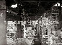 681_372a Im Lagerhaus C des Melniker Ufers im Hamburger Moldauhafen sind mit Bandeisen verschnrte Wollballen bis unter die Decke des Speichers gelagert. Licht fllt ber die Oberlichter auf die Gter - fr den Nachtbetrieb hngen Lampen an der Decke ber dem Gang.