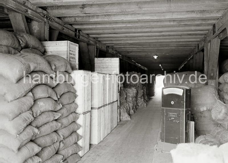 Historische Bilder der HHLA von der Warenlagerung im Hamburger Freihafen. Warenlagerung auf einem Speicherboden - Gter in unterschiedlicher Verpackung; ca. 1934.  685_622 Waren in unterschiedlicher Verpackung werden auf einem Speicherboden im Freihafen Hamburgs gelagert. Rechts eine bewegliche Waage der Fa. Dinse-Maschinenbau AG, die auf Rdern an ihren Arbeitsplatz gerollt werden kann.