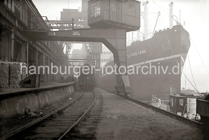 Historische Hafen- Bilder aus dem Archiv der Hamburger Hafen und Logisitk AG. Gterumschlag  am Hafenkai / Gterzug an der Laderampe, Frachtschiff.  688_B_326a Ein Gterzug steht auf den Schienen der Hafenbahn an der Laderampe des Kaischuppens - Kaiarbeiter transportieren mit ihren Sackkarren Ballen in den Schuppen. Ein chinesischer Frachter liegt an der Kaimauer.