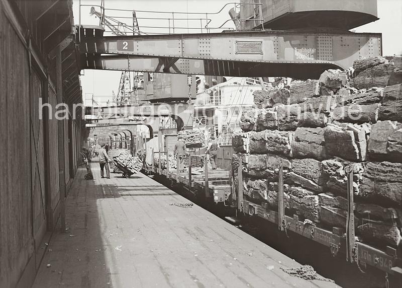 Bilddokumentation zur Geschichte des Hafen Hamburgs aus dem Archiv der HHLA. Beladung eines Gterzugs mit einer Ladung Kork;  ca. 1938.  697_654 Ein Gterzug wird mit dem Rohstoff Kork im Hamburger Hafen beladen; die Rinde der Korkeiche wird hoch auf den offenen Gterwaggons an der Rampe gestapelt. Ein Kaiarbeiter fhrt eine Sackkarre mit einer Fuhre Kork an den Waggon heran whrend zwei Hafenarbeiter eine Hieve des Krans entgegen nehmen.