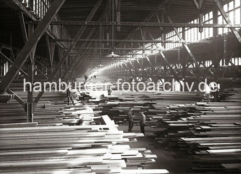 Fotodokumentation zur Geschichte des Hamburger Hafens. Lagerung von Bohlen und Brettern im Schuppen 44, Hansahafen.  698_154 Arbeiter stapeln Holzbretter im Schuppen 44 des Hamburger Hansahafens am O'Swaldkai. Die Lagerarbeiter mssen auf die Holzstapel klettern, um die Bohlen von Hand auf den Stapel zu legen. ber die Oberlichter fllt das Tageslicht in den langgestreckten Kaischuppen - fr den Nachtbetrieb hngen Lampen von der Decke des Lagerschuppens.