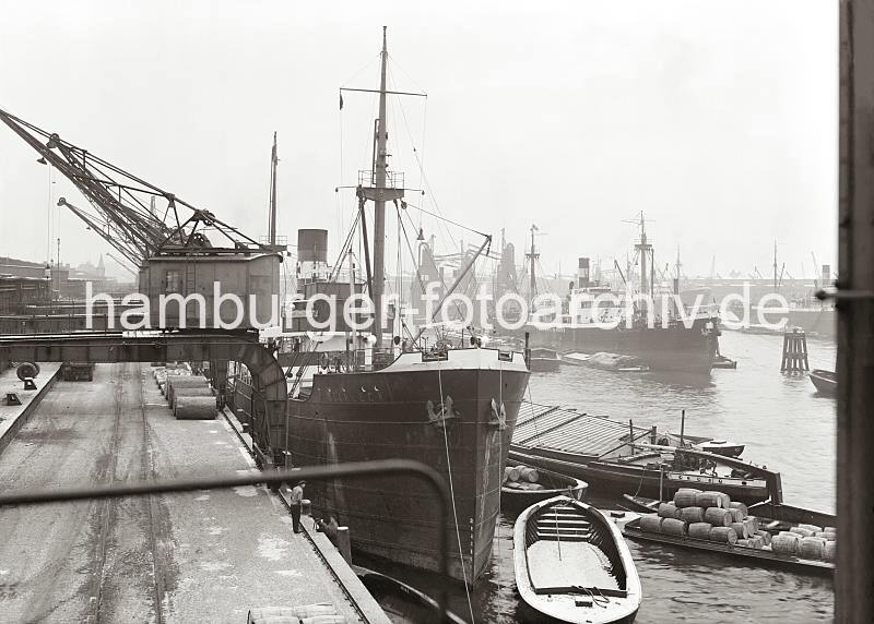 Historische Hafenszenen aus dem Hamburger Hafens - Motive aus dem Archiv der HHLA. Frachtschiff am Hafenkai - Schuten mit Ladung. 700_700a Die Ladung eines Frachters wird auf die lngsseits liegenden Schuten gelscht - einer der Lastkhne ist mit Holzfssern hoch beladen. Am Kai liegen fr den Weitertransport in Stcke aufgeteilt Stmme tropischer Bume.