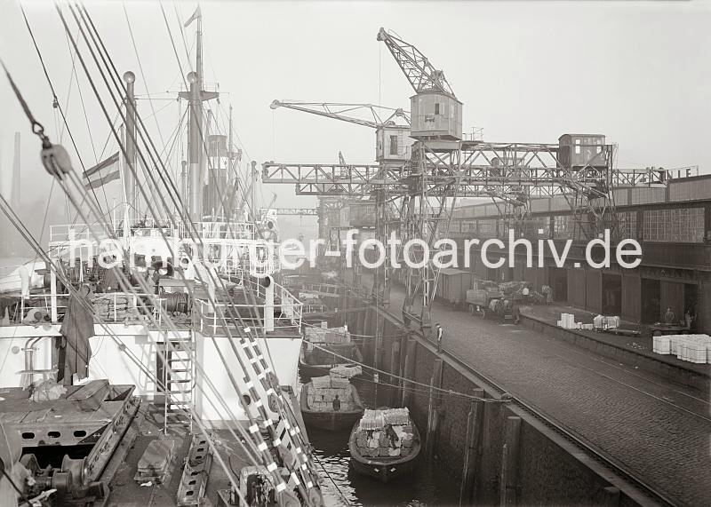 Historische Archivfotos der Hamburger Hafen und Logistik AG (HHLA)Warenumschlag am Kai des Hafen Hamburgs; ca. 1934.  704_583a Frachter liegen abgebumt am Hafenkai: mit Baumstmmen und Holzbohlen wird zwischen Kaimauer und Schiffswand ein Abstand gehalten, damit Schuten dazwischen liegen und beladen oder entladen werden knnen.  Mit dem Kran werden Wollballen auf die Lastkhne verladen - die Ewerfhrer klettern auf der Ladung um die Ballen in die richtige Position zu bringen. Auf dem Kai stehen Gterwaggons und ein Pferdefuhrwerk - dessen Kutscher hat die beiden Zugtiere in der Wartezeit mit schtzenden Decken versehen.
