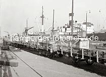 707_545b Beladenen Gterwaggons stehen am Holthusenkai; auf den Holzkisten sind die Aufschriften des Bestimmungsortes der Gter BUENOS AIRES sowie die Herkunft PRODUCCION ALEMANA zu erkennen. Zwei Hafenarbeiten stehen auf der Ladung und bereiten die Verladung auf das Schiff vor; lks. steht auf dem Gleis ein Schleppwagen, mit dem ein Gterwaggon ohne die Hilfe einer Lokomotive von einem Arbeiter bewegt werden kann.  Hinter den Schiffsaufbauten ist rechts der Turm der Nikolaikirche zu erkennen.