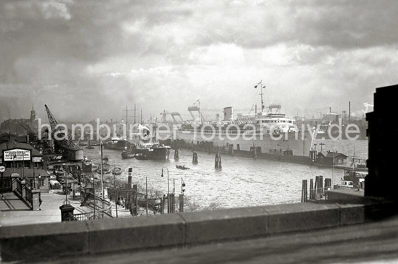 Historische Hamburg-Bilder - Frachtschiffe im Hamburger Niederhafen, Johannisbollwerk + Vorsetzen - Passagierschiff Wilhelm Gustloff. 709_364 Blick von der Hochbahnstation Landungsbrcken auf den Niederhafen und Johannisbollwerk. Lks. die Kaischuppen der Hamburg Rhein Linie - unter den Halbportalkrnen stehen Lastwagen an der Rampe. Binnenschiffe und Schuten haben am Kai fest gemacht. Im Hintergrund das Dach und der Turm des Kaispeichers A. Am Ponton liegt das 1937 gebaute Passagierschiff Wilhelm Gustloff, das von der national- sozialistischen Organisation "Kraft durch Freude Kdf" als Kreuzfahrtschiff genutzt wurde.