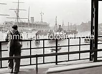 711_386 Ein Hafenarbeiter steht am Gelnder der berseebrcke und blickt auf die Schiffe im Hamburger Niederhafen. Einige der Frachter liegen an den Holzdalben, andere Schiffe an der Kaimauer der Rhein Maas Schuppen am Johanisbollwerk. Links das Jugendherbergsschiff HEIN GODENWIND und das KdF Passagierschiff Wilhelm Gustloff. Im Hintergrund die Kuppeln der St. Pauli Landungsbrcken.