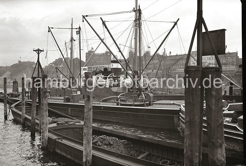 Fotoposter von Hamburg als Geschenk fr die Firma + Buero : Schuten an Holzdalben - Gebude an den Vorsetzen. 716_B_230 Zwei Schuten liegen an den Holzdalben beim Johannisbollwerk, die Schiffstaue sind so um die Holzpfhle gelegt, dass die Lastkhne sich mit der Tide bewegen knnen. Dahinter wird gerade eine Hieve Scke von einem Kstenmotorschiff auf ein Binnenschiff verladen.