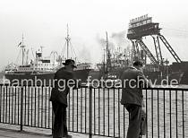 722_3 Schaulustige stehen auf den Landungsbrcken und sehen dem Schiffsverkehr auf der Elbe zu - der Frachter SANTA CATRARINA wird von dem Schlepper W. TH. STRATMANN aus dem Hamburger Hafen geschleppt. Im Dock der Stlckenwerft liegt ein Schiff zur Reparatur - an dem Portal der Kabelkrananlage ist der Schriftzug der 1840 gegrndeten Hamburger Werft angebracht.