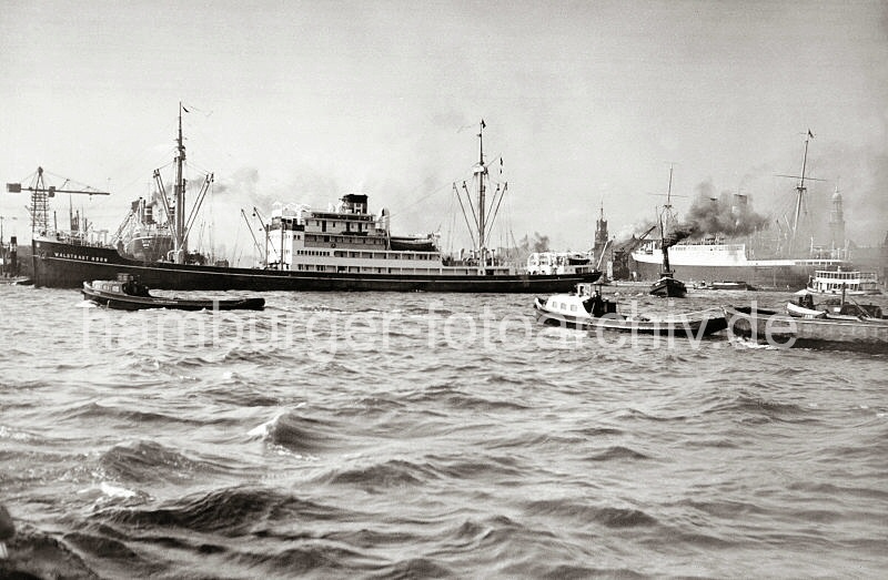 Historische Schiffsfotografien - Wendemanver auf der Elbe vor dem Strandhafen; Barkassen + Schlepper; ca.1937.  738_B_309 Der Frachter WALTRAUD HORN bei seinem Wendemanver auf der Elbe vor dem Strandhafen - zwei Hafenschlepper untersttzen das Seeschiff bei der Aktion. Barkassen und ein Schleppzug warten darauf, dass die Durchfahrt wieder frei ist. Im Hintergrund re. der Turm des Michels und der Uhrturm vom Kaispeicher A.