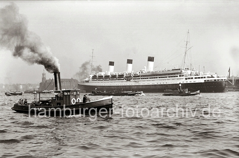 Historische Schiffsfotos - Hafenschlepper unter Dampf - Passagierschiff CAP ARCONA im Strandhafen; ca.1937.  739_B_308a Der Passagierdampfer CAP ARCONA liegt vertut an den Dalben des Strandhafens; der Luxusdampfer lief 1927 vom Stapel. Das 196m lange Passagierschiff hat eine Breite von ca. 26m und konnte 850 Passagiere an Bord nehmen (1937). Im Vordergrund ein Hafenschlepper unter Dampft - dahinter das Gebude des Kaispeichers A am Kaiserhft.