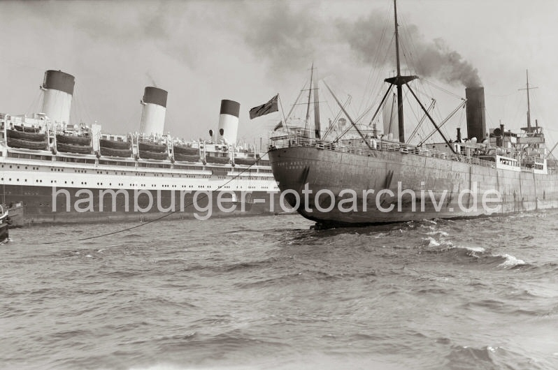 Historische Schiffsmotive - Frachtschiff auf der Elbe - Schornsteine der CAP ARCONA; ca.1937.  739_398 Das britische Frachtschiff PORT ADELAIDE mit Schlepperhilfe auf der Elbe - Qualm steigt aus dem Schornstein des Schiffs. Dahinter die drei markanten Schornsteine des Flaggschiffs der Hamburg Sdamerika Linie, das Passagierschiff CAP ARCONA.