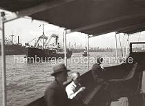 756_3_614 Blick vom Fahrgastraum einer Hafenfhre auf die Elbe - das Frachtschiff OLDENBURG luft in den Hafen Hamburgs ein. Die Ladung ist hoch an Deck des Frachters gestapelt. Am Elbufer von Steinwerder ragen die Portale der Kabelkrne der DEUTSCHEN WERFT empor - Schiffe liegen zur Reparatur und berholung in den Docks.