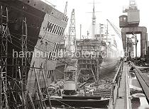 758_631 Schwimmdock der 1877 gegrndeten Werft Blohm & Voss - Werftkrne stehen am Rand des Docks und transportieren Arbeitsmaterial zum Schiff. Im Vordergrund liegen ein Schwimmkran und eine Arbeitsschute an der Stirnseite der Dockanlage.